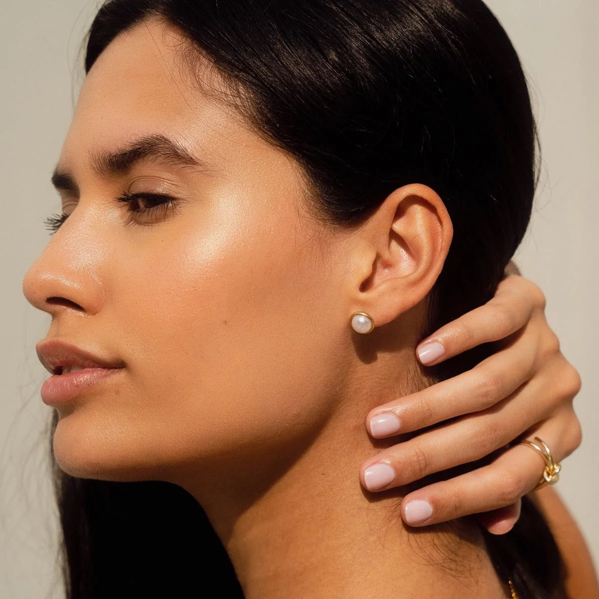 Aros stud dorados con perla redonda blanca en engaste liso, baño de oro 18K sobre acero inoxidable 316L.