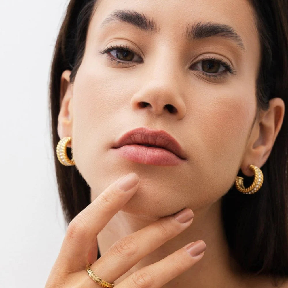 Aros dorados de media argolla con textura trenzada y fila central de circonias, baño de oro 18K en acero inoxidable 316L.